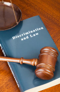 The picture shows a book titled "Discrimination and Law" and a gavel, with a cherry-wood desk underneath them.